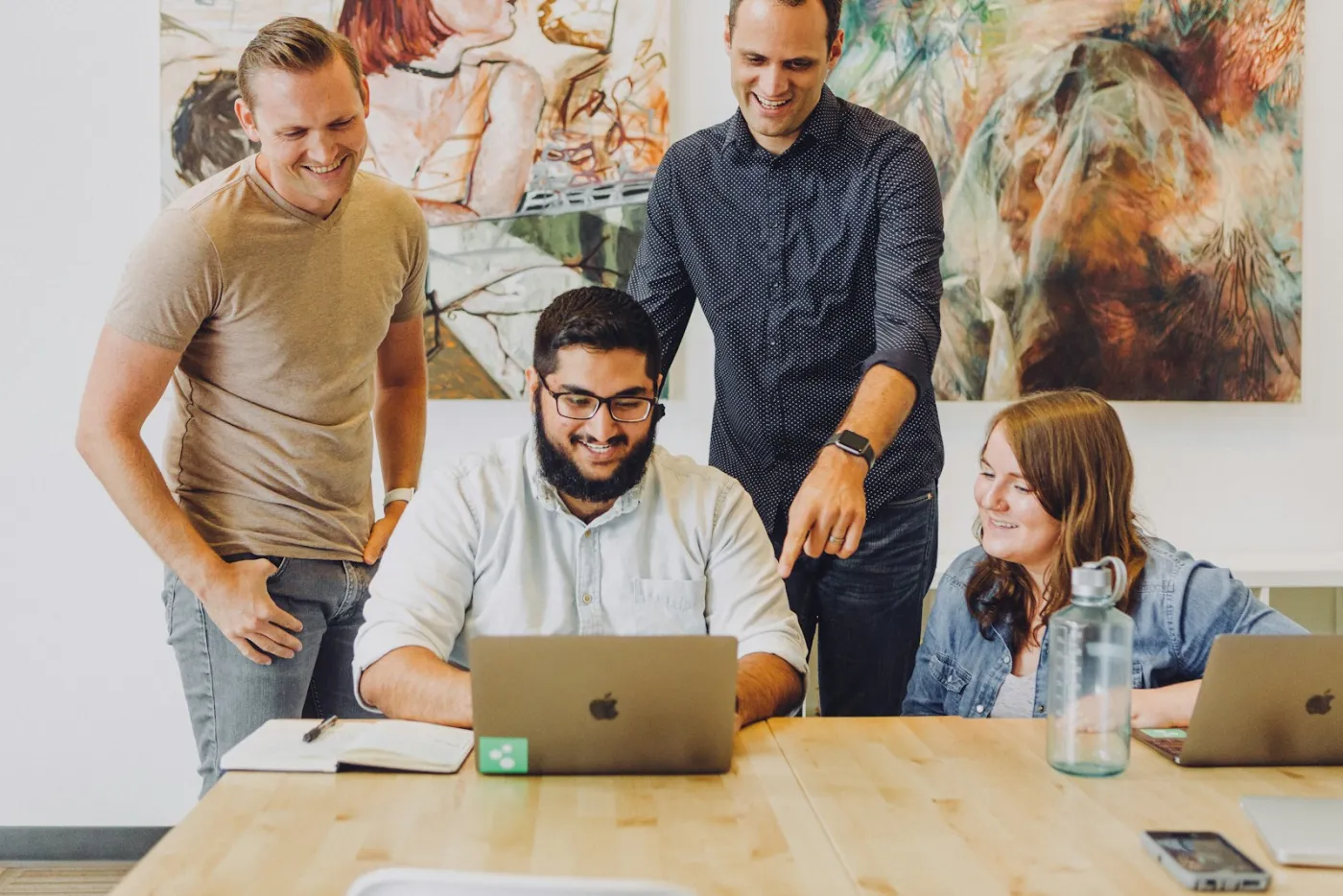 Four colleagues smiling round a laptop while one points at the answer on screen